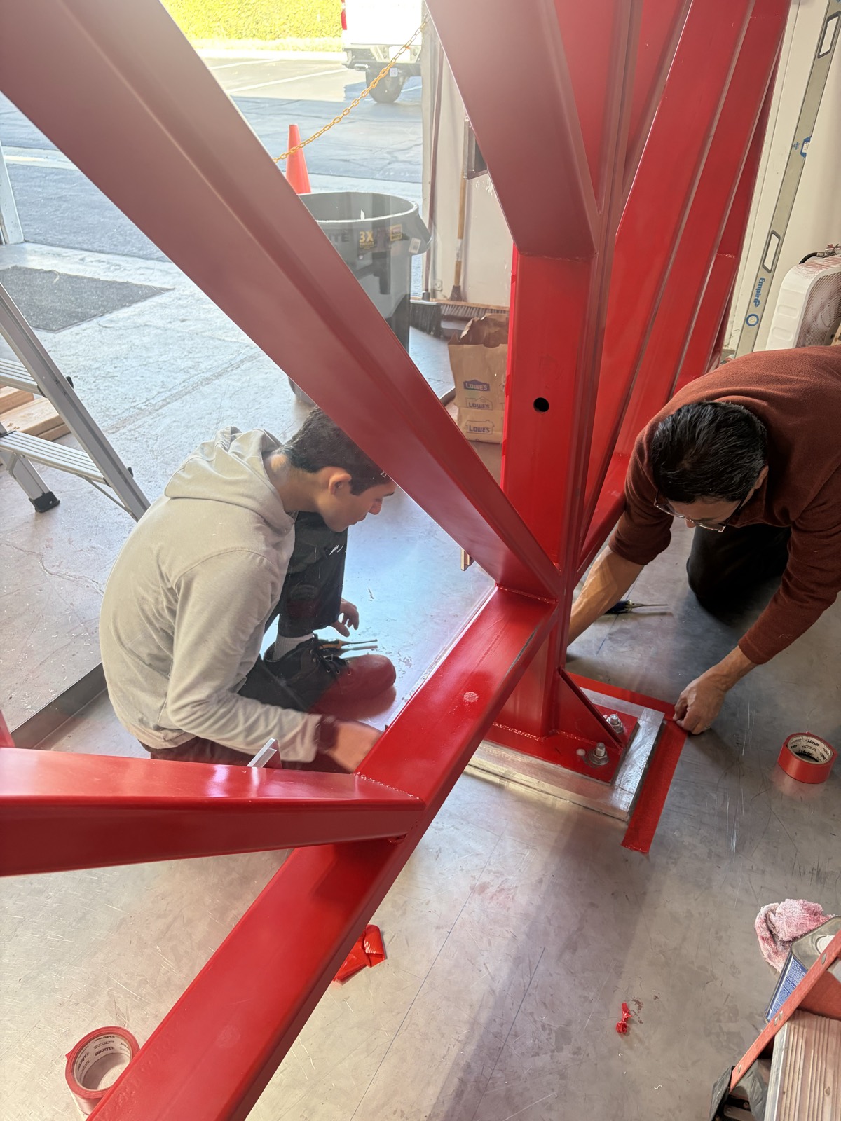 Two technicians taping and sealing the base plates of the red steel pressure test wall